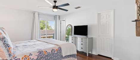 A bedroom with a bed, a dresser, a television, and a ceiling fan.