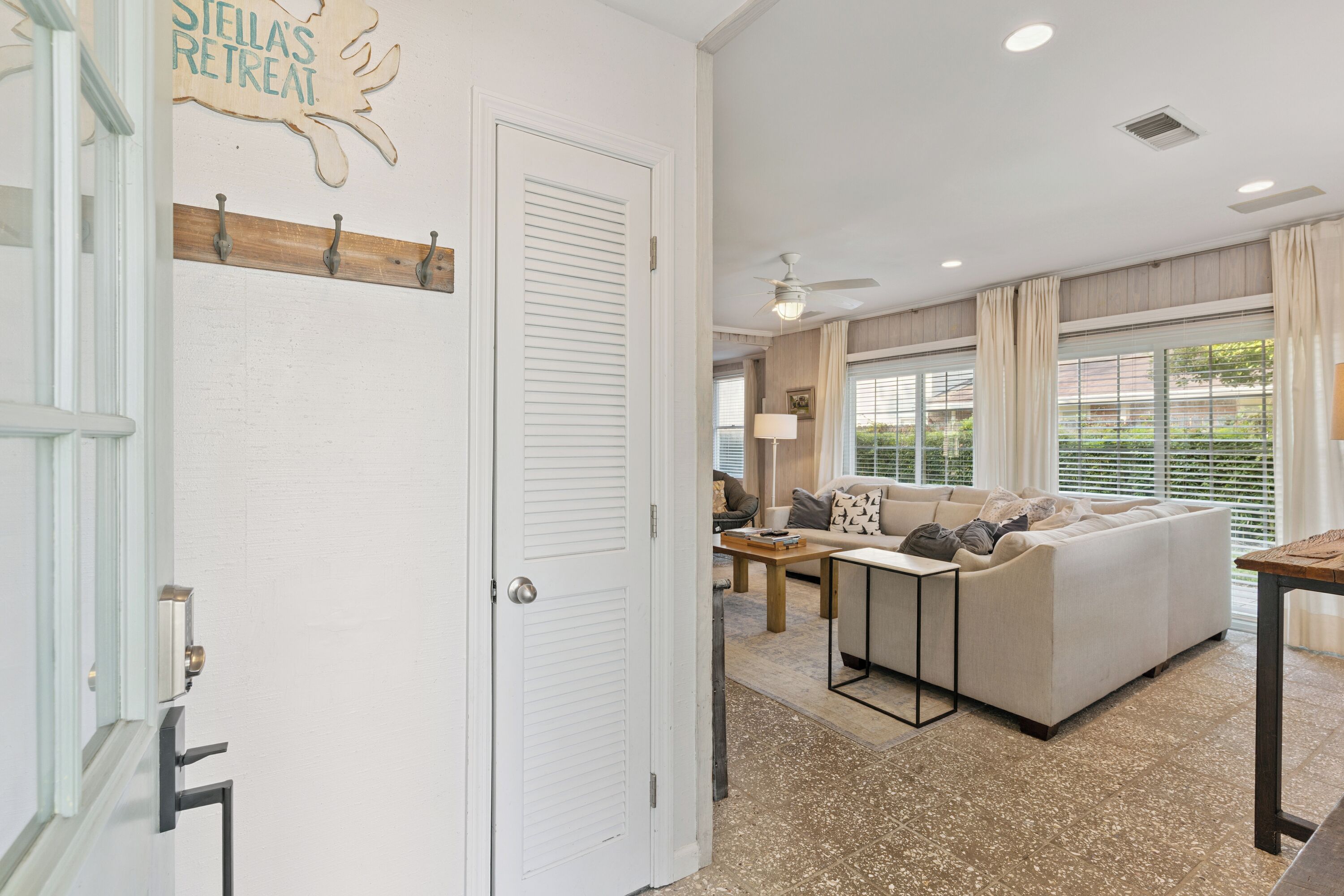 A spacious living area with a sofa, a coffee table, and a dining table. There is a door with a sign above it and a ceiling fan.