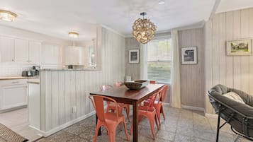A kitchen with white cabinets, a wooden island, and a dining table with orange chairs.