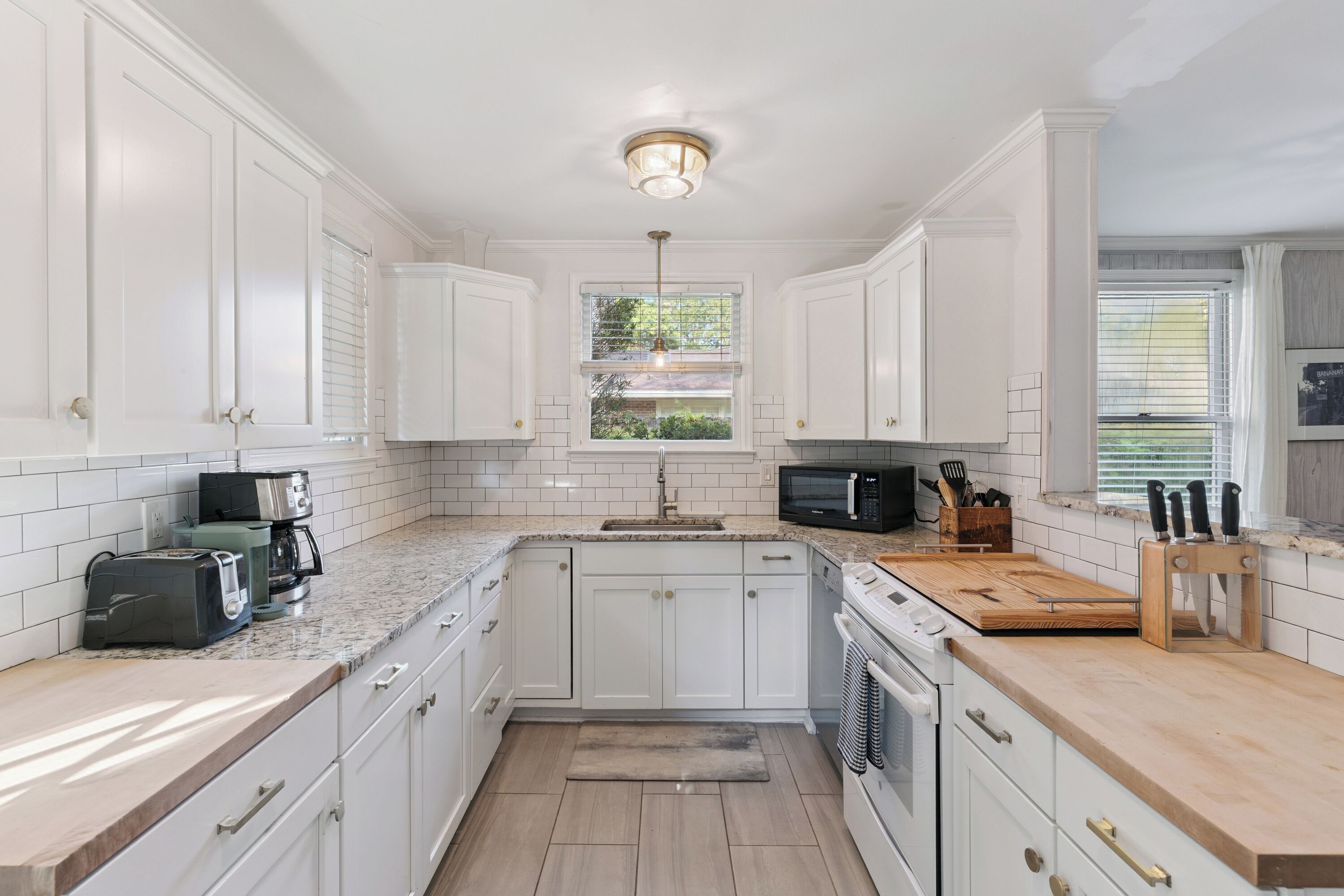 A kitchen with white cabinets, a granite countertop, a built-in oven, and a window with blinds.