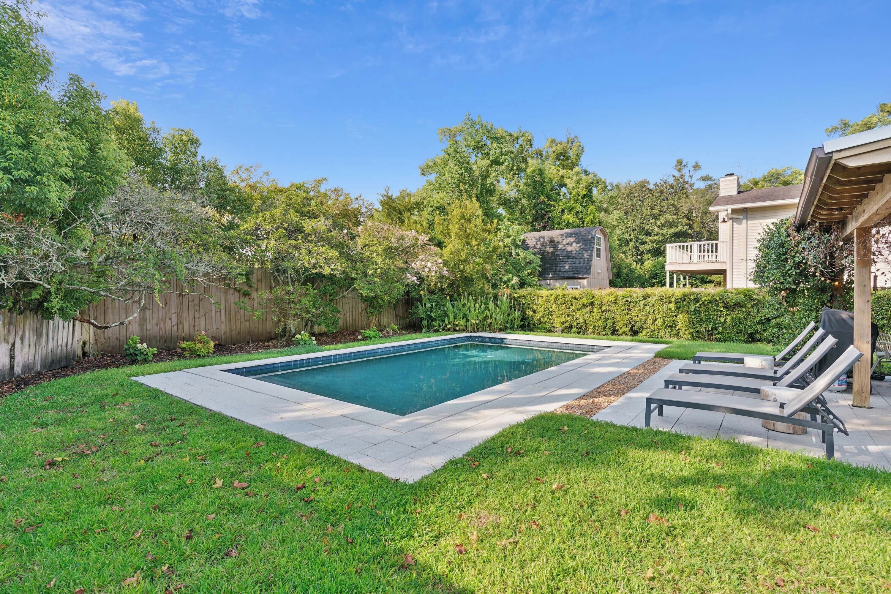 A backyard with a swimming pool, a wooden deck, and a fenced area.