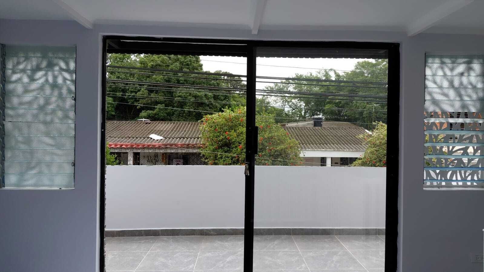 Quarto com porta de correr de vidro que dá para uma varanda com vista para edifícios e árvores vizinhas.