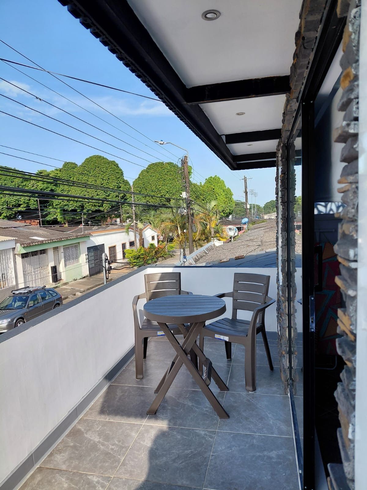 Uma varanda com mesa e cadeiras, vista para a rua e um edifício com telhado em azulejos.