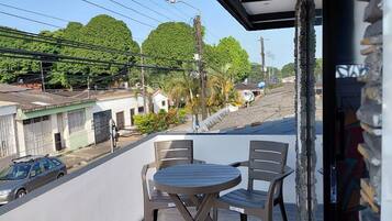 A balcony with a table and chairs, a view of the street, and a building with a tiled roof.