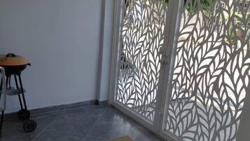 Une pièce avec un sol carrelé, une porte blanche ornée de motifs découpés, un luminaire fixé au mur et une petite table avec une chaise.