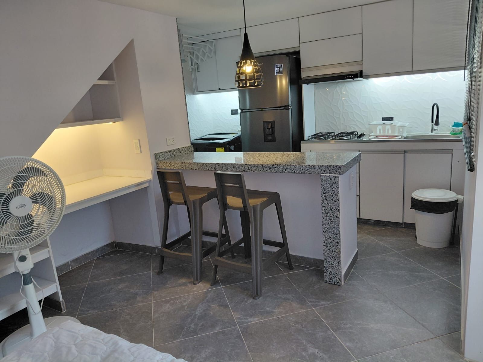 A compact kitchen with a central island, two bar stools, a built-in fan, and a gas stove.