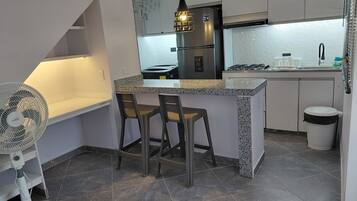 A compact kitchen with a central island, two bar stools, a built-in fan, and a gas stove.