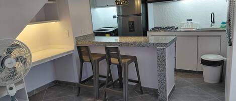 Una cocina compacta con una isla central, dos taburetes de bar, un extractor empotrado y una estufa a gas.