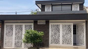 A modern two-story building with decorative white panels on the facade, a balcony, and a small tree in the foreground.