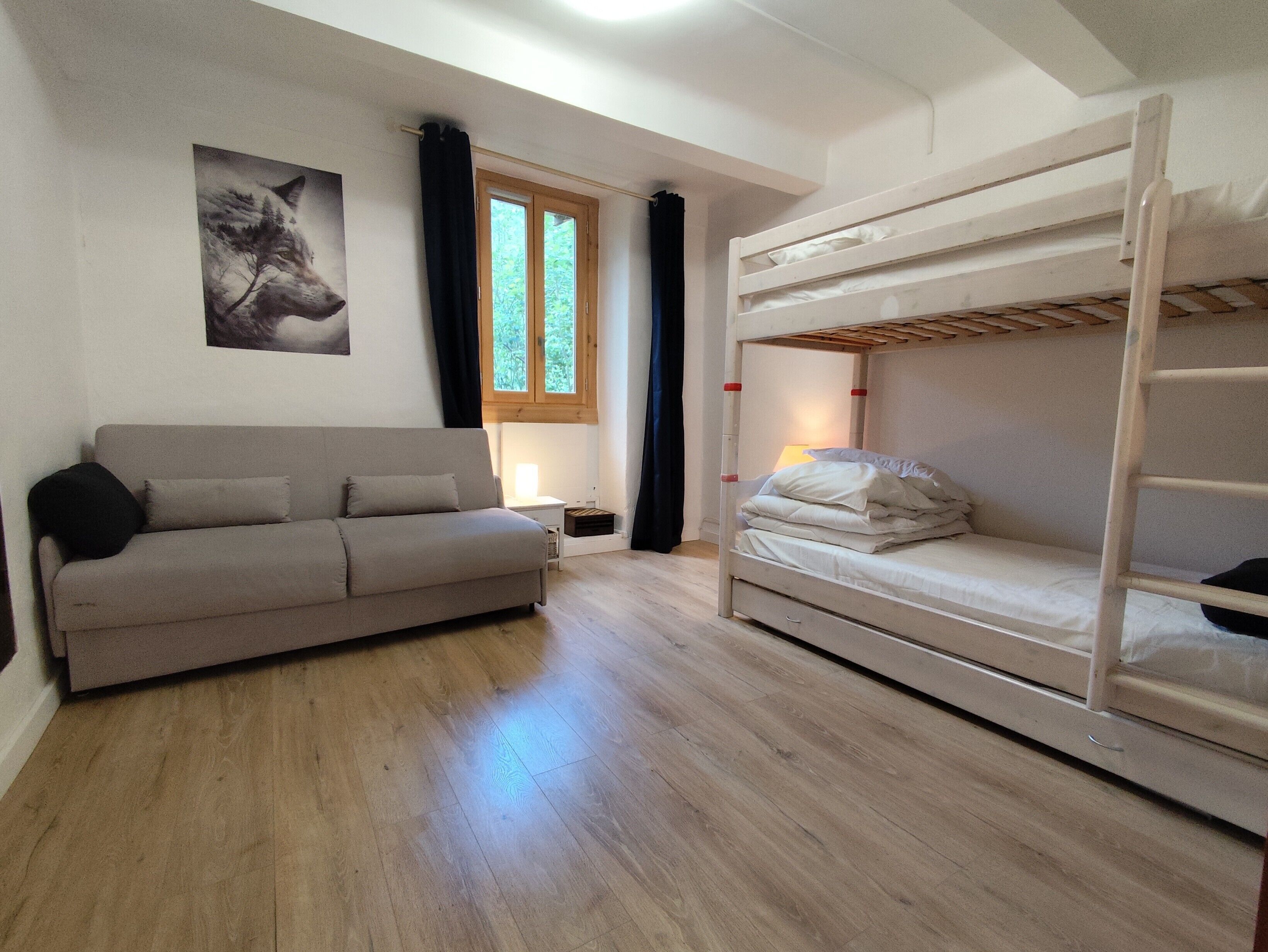 Una habitación con literas, un sofá, una ventana con cortinas e imagen colgada en la pared.