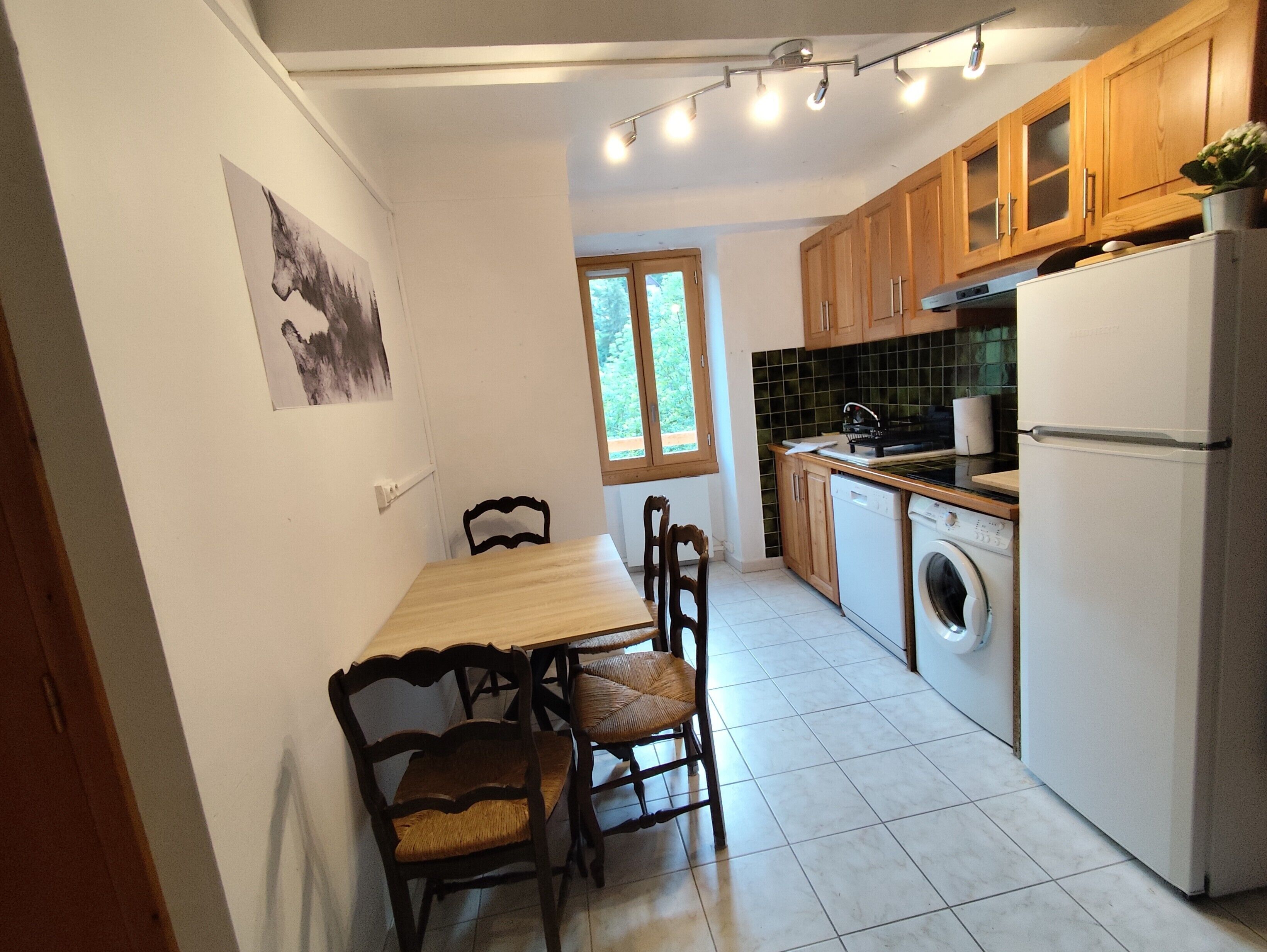 Une cuisine compacte comprenant une table à manger, des chaises, un lave-linge et un réfrigérateur.