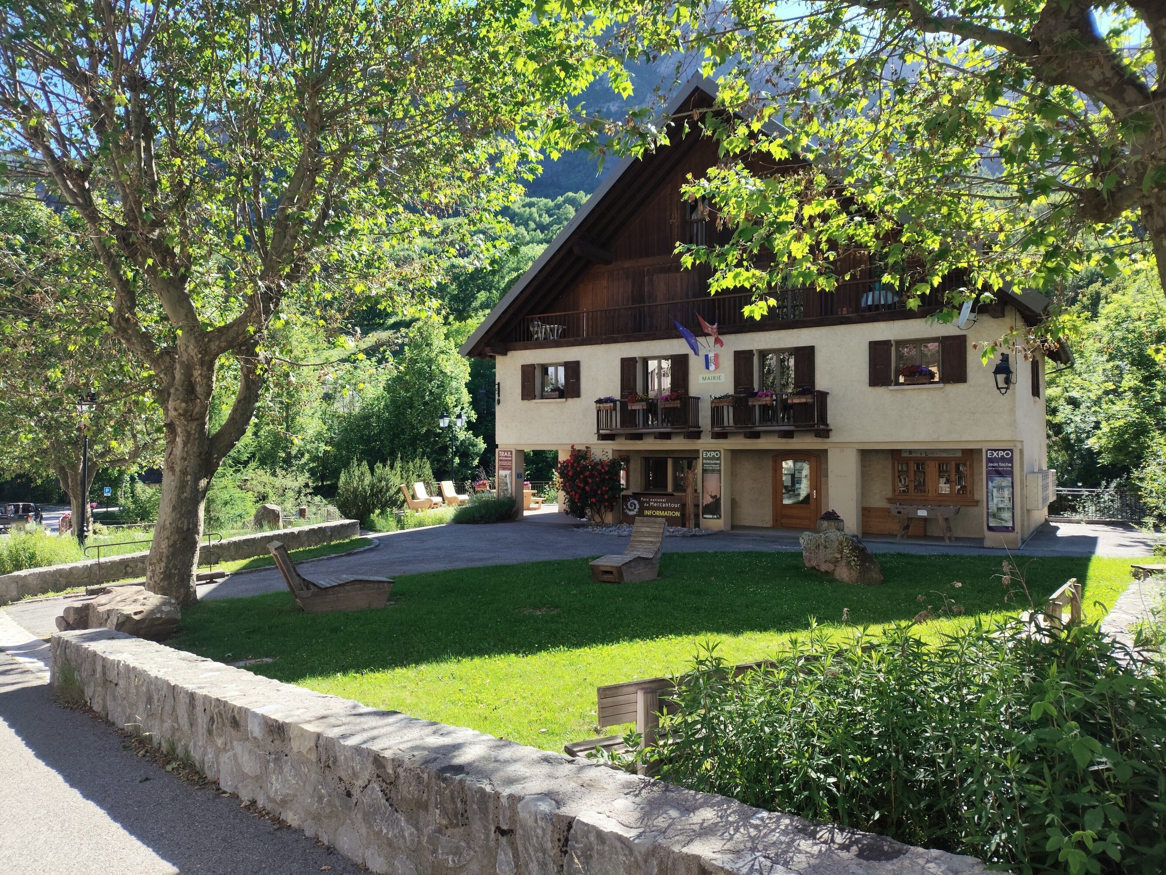 A two-story building with a balcony, a sign reading 'MAIRIE,' and a paved area with benches.