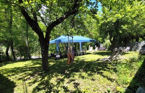 A shaded outdoor area with a blue canopy, surrounded by trees and grass.