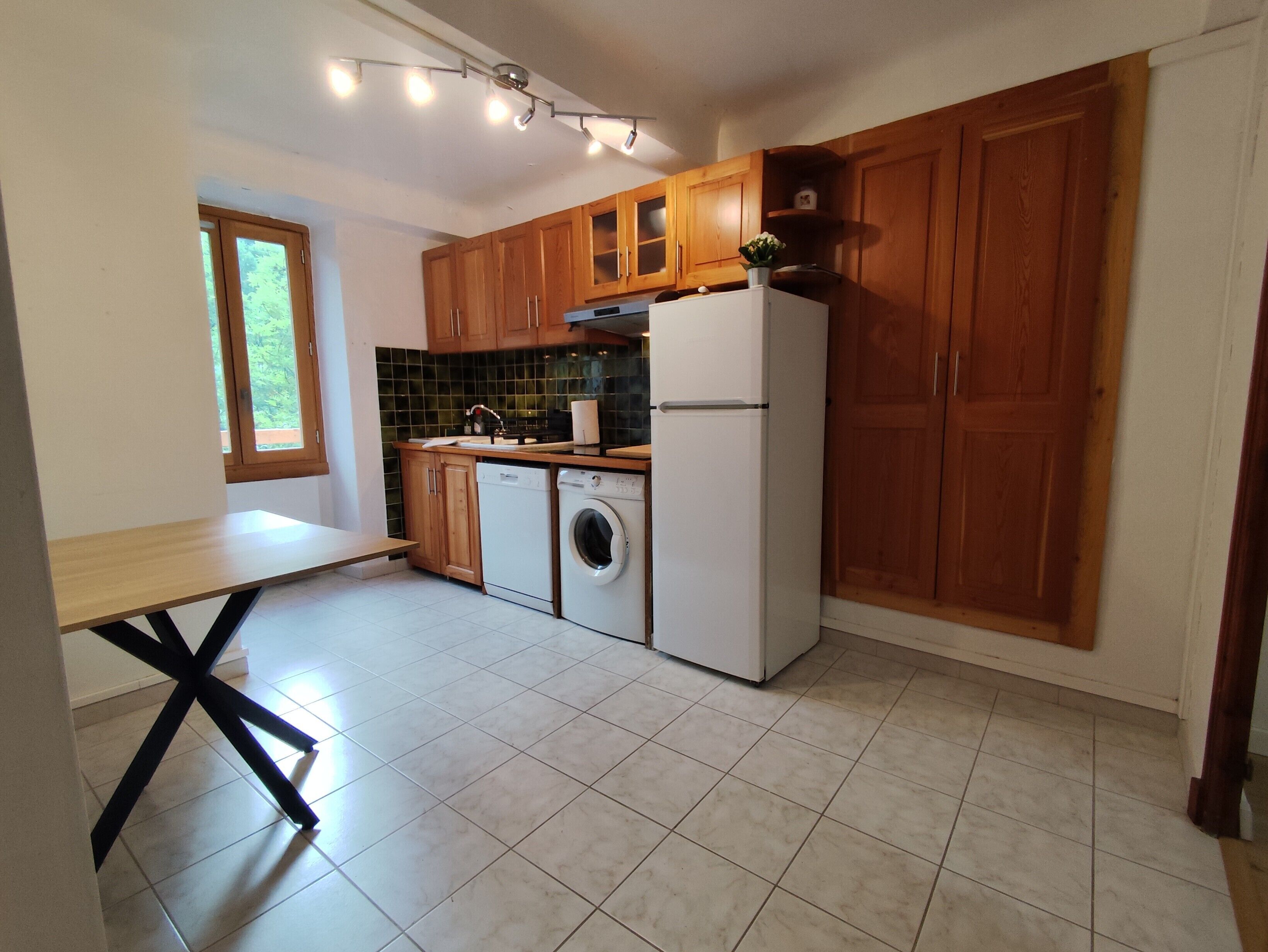 Eine Küche mit Holzausstattung, einer Waschmaschine, einem Kühlschrank und einem Esstisch.