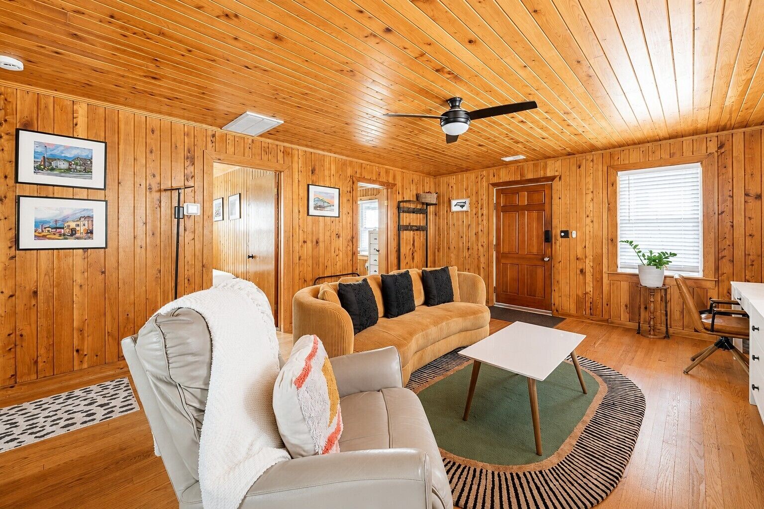 Interior acogedor de una cabaña con techo de madera, un sofá, una silla, una mesita y una ventana con persianas.