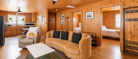 Interior acogedor de una cabaña con detalles de madera, un sofá, una mesa de comedor y una zona de cocina.