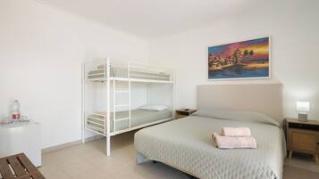 Un dormitorio con una cama litera, una cama individual, una mesita de noche con una lámpara y un cuadro en la pared.