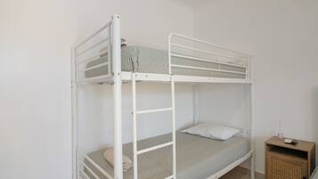 A bunk bed with a lower bunk and a single bed, a small wooden nightstand with a lamp, and a wall-mounted shelf.