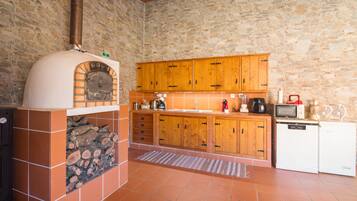 Una cocina con pared de piedra, armarios de madera, horno empotrado y un refrigerador pequeño.