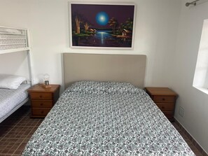 Een slaapkamer met een bed, twee nachtkastjes, een lamp, een schilderij van een nachtscène en een raam.