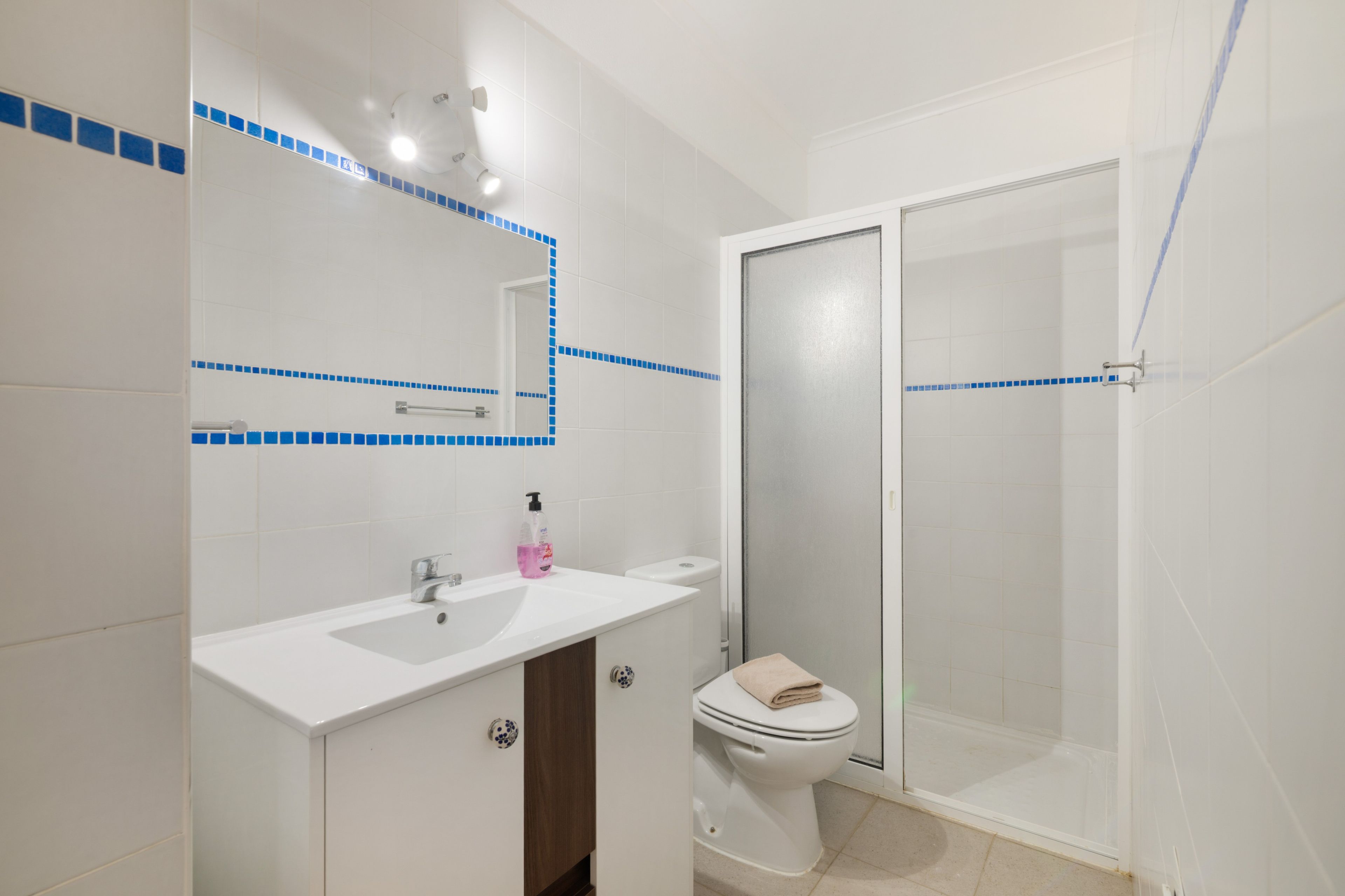 A bathroom with a white sink, a mirror, a toilet, and a shower area.