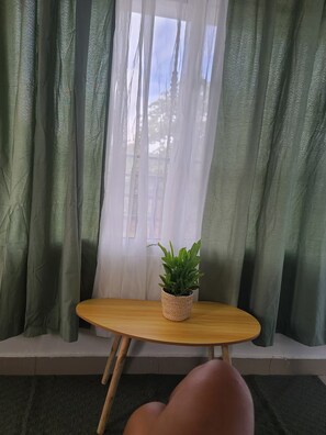 Ein Zimmer mit Fenster, einem kleinen Tisch mit Pflanze und einem Stuhl.