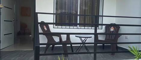 A balcony with a table and chairs, a window with bars, and a small garden area with plants.