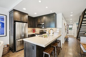 A modern kitchen with dark wood cabinets, stainless steel appliances, and a central island with stools. - Three Kings Remodeled Townhome Walk to Ski 2BR/2BA Spa Inspired Primary Suite (Park City)