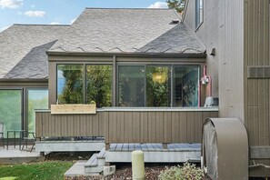 Una casa moderna con ventanas amplias, un porche cubierto y una unidad de aire acondicionado visible.