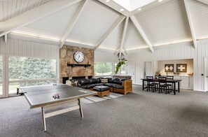 A spacious room with a ping pong table, a stone fireplace, a leather sofa, and a dining area with a kitchen in the background. - Three Kings Remodeled Townhome Walk to Ski 2BR/2BA Spa Inspired Primary Suite (Park City)