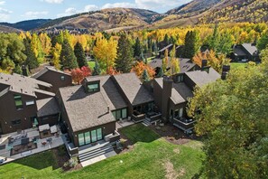 A modern residential area with multiple houses featuring sloped roofs and large windows, surrounded by autumn-colored trees and hilly terrain in the background. - Three Kings Luxury Townhome 2BR Walk to Ski - Spa Inspired Bath (Park City)