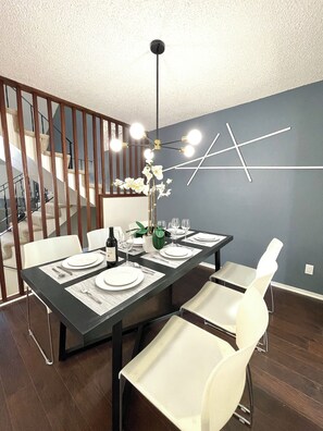A modern dining area with a dark wooden table, white chairs, and a contemporary light fixture. - South San Francisco Sweet Home-10 minutes to SFO (South San Francisco)