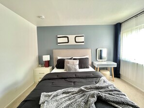 Une chambre à coucher moderne avec un grand lit, des tables de chevet, une lampe de chevet, un miroir et une fenêtre avec des rideaux.