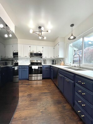 A modern kitchen with stainless steel appliances, dark blue cabinets, and a large window providing natural light. - South San Francisco Sweet Home-10 minutes to SFO (South San Francisco)
