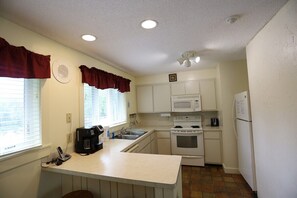 A compact kitchen with white cabinets, a microwave, stove, and a refrigerator. - Inns of Waterville Valley 2 bedroom (Waterville Valley)