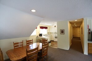 A dining area with a wooden table and chairs, a kitchen with white cabinets, and a hallway leading to another room. - Inns of Waterville Valley 2 bedroom (Waterville Valley)
