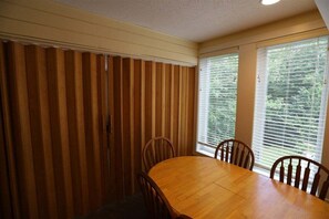A dining area with a wooden table and chairs, large windows with blinds, and a ceiling light. - One Bedroom with 2 living rooms at Inns of WV! (Waterville Valley)