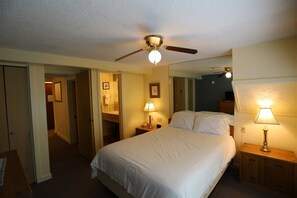 A hotel room with a bed, a ceiling fan, a nightstand with a lamp, and a mirror on the wall. - One Bedroom with 2 living rooms at Inns of WV! (Waterville Valley)