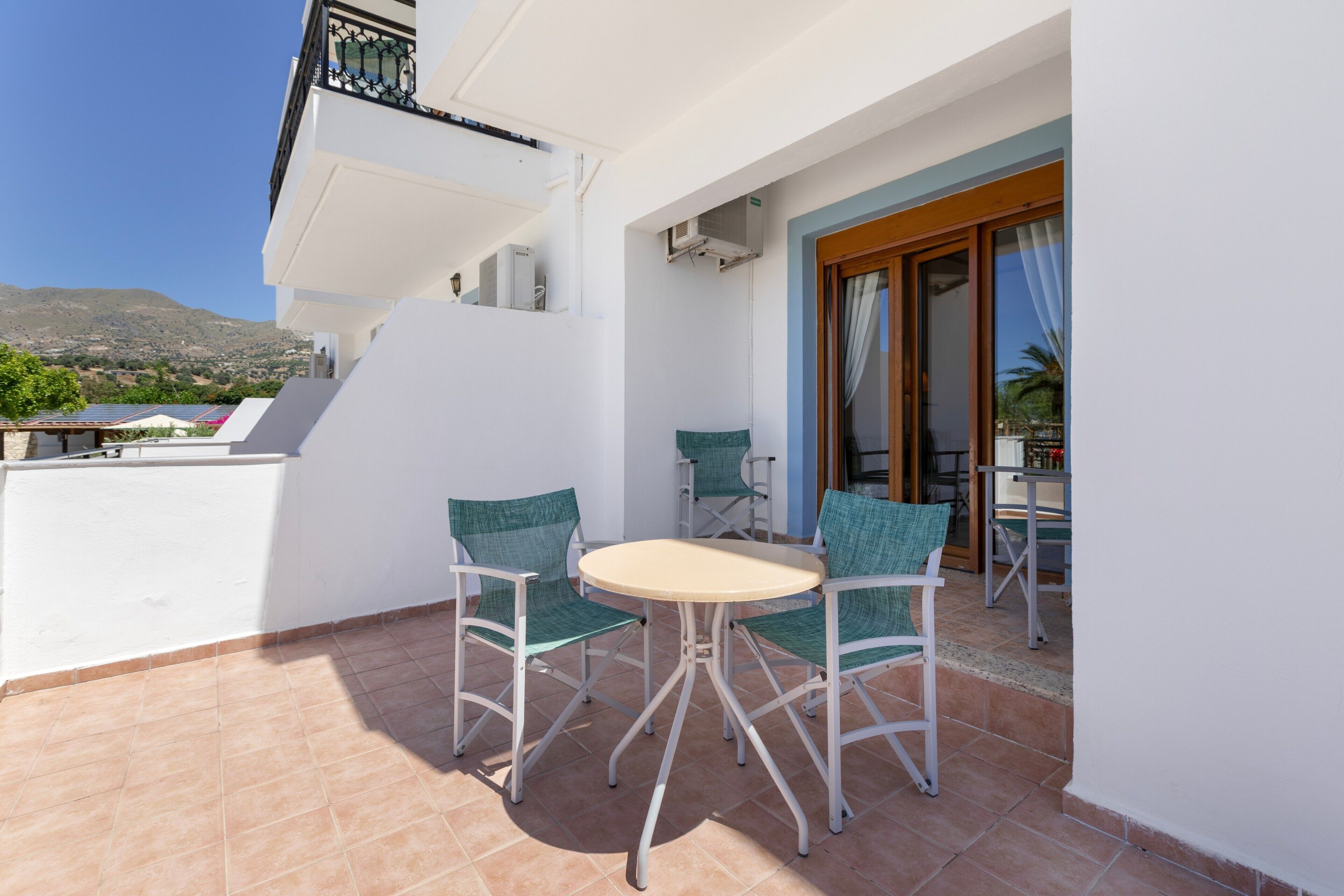 Ein Balkon mit rundem Tisch und vier Stühlen, Blick auf die Landschaft, sowie ein Gebäude mit einem Balkon.