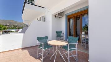 A balcony with a round table and four chairs, a view of the landscape, and a building with a balcony.