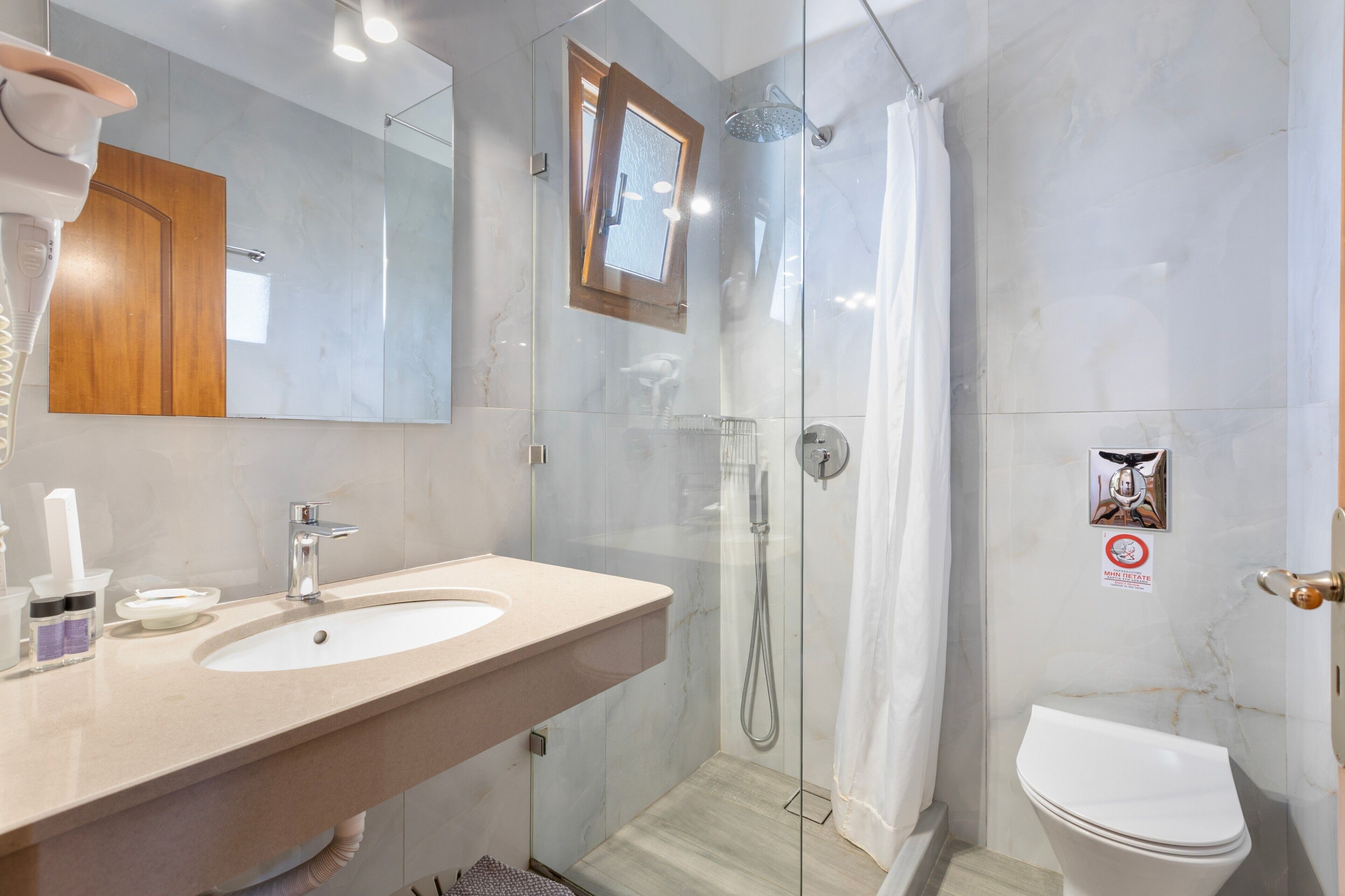 Ein modernes Badezimmer mit einer gläsernen Duschkabine, einem Waschbecken inklusive Spiegel und einer Toilette.
