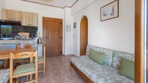 Un espacio habitable compacto con kitchenette, una mesa de comedor de madera con sillas, un sofá con cojines y un cuadro en la pared.