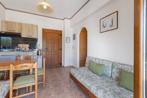 Ein gemütlicher Wohnbereich mit einer Küchenzeile, einem Holztisch mit Stühlen, einer Couch mit Kissen und einem gerahmten Bild an der Wand.