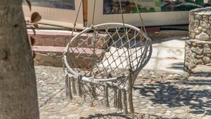 Una silla mecedora de mimbre con asiento y respaldo de cuerda, ubicada sobre un pavimento de adoquines.