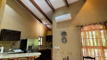 Una cocina con ventilador de techo, refrigerador, cafetera y ventana con cortinas.