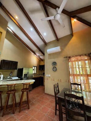 A kitchen with a ceiling fan, a refrigerator, a coffee maker, and a window with curtains.