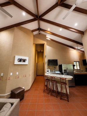 A kitchen with a central island, bar stools, a refrigerator, and a ceiling fan.