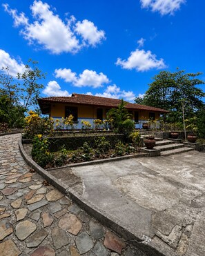 A building with a tiled roof, surrounded by a garden with various plants and a stone pathway.