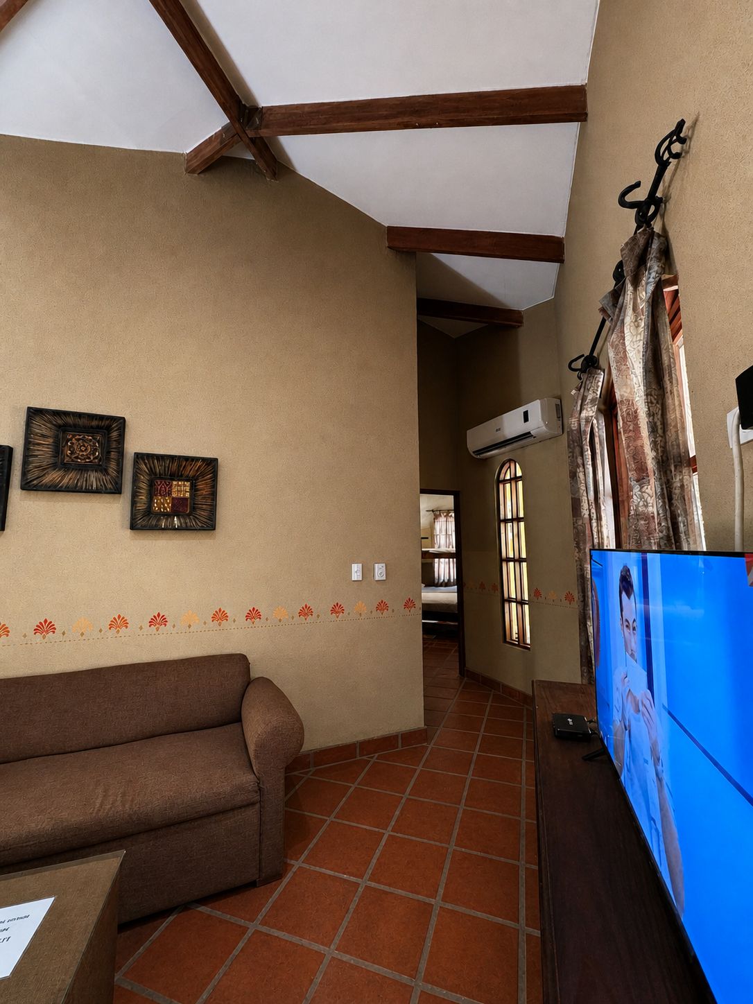 A living room with a sofa, a television, and a wall-mounted air conditioning unit.