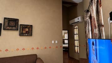 A living room with a sofa, a television, and a wall-mounted air conditioning unit.